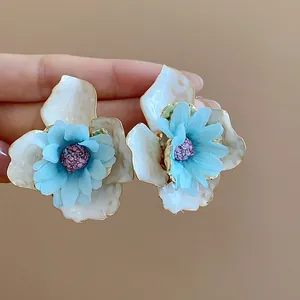 Dettaglio degli orecchini a lobo con fiori in tessuto blu, petali in smalto crema e centro viola.