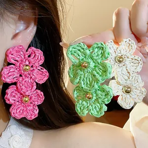 Close-up of vibrant handmade woven raffia double flower drop earrings worn by a model