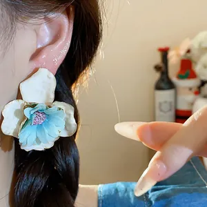 Primo piano di eleganti orecchini a fiore in tessuto bianco e blu su una modella.