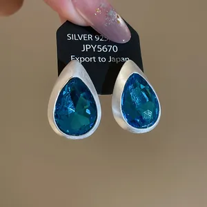 Close-up of vintage teardrop earrings with blue crystals and brushed silver metal finish.