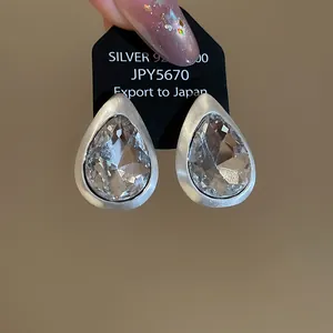 Macro view of vintage teardrop crystal stud earrings with brushed silver metal finish.