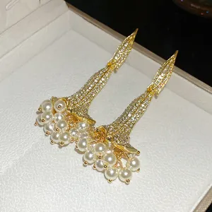 Dettaglio di eleganti orecchini pendenti color oro con strass e grappoli di perle.