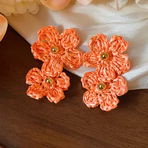 Detailed view of handmade orange raffia flower earrings with golden bead centers