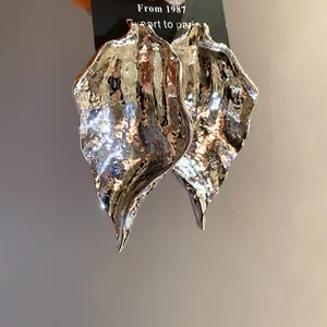 Macro detail of silver-toned hammered metal leaf earrings on a black display card