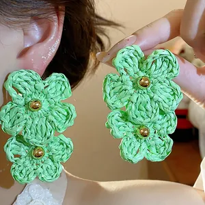 Detailed view of light green woven raffia flower earrings with golden bead centers