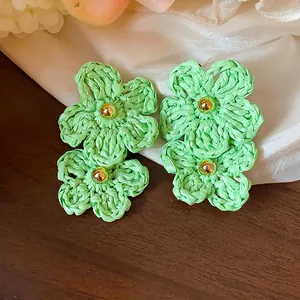 Detailed view of handmade light green raffia flower earrings with golden bead centers