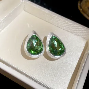 Macro view of vintage brushed silver stud earrings featuring faceted green teardrop gemstones