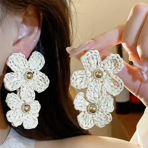 Detail of hand-woven raffia flower earrings with gold bead centers on model