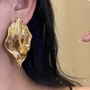 Close-up detail of large textured gold leaf earrings with a unique hammered finish