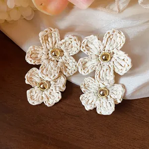 Macro detail of elegant woven raffia flower drop earrings with gold center beads