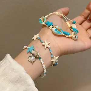 Stacked blue shell and starfish beaded bracelets on wrist for beach vacation style.