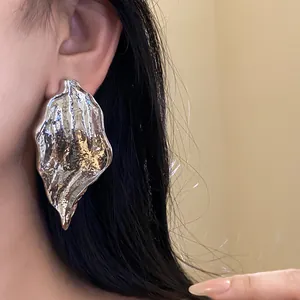 Detailed close-up view of stylish silver wrinkled leaf drop earrings on model ear.