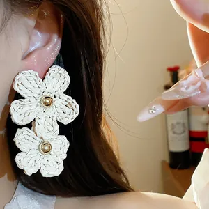 Detailed close-up showing textured cream woven raffia flower earrings worn by a model