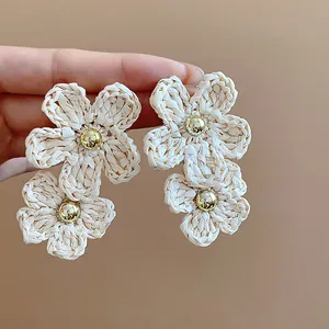 Macro view of handmade woven beige raffia flower drop earrings with a central gold bead.