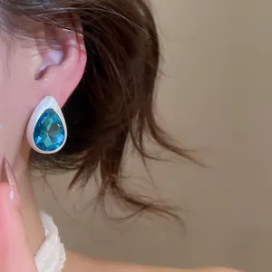 Close-up of vintage teardrop earrings featuring a faceted blue rhinestone on brushed metal