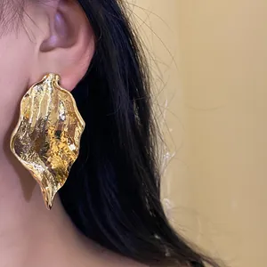 Close-up detail of a large gold crumpled leaf earring showing metallic texture and scale