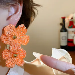 Detailed close-up view of orange raffia woven flower stud earrings on model's ear