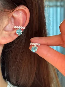 Detailed macro view of sparkling light blue square zircon ear cuff on human ear and fingers
