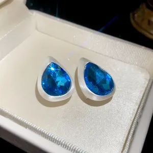 Detailed close-up of blue teardrop stud earrings with brushed silver finish in box