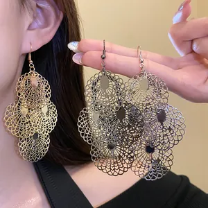 Detail view of large hollow-out metal drop earrings in gold and silver boho fashion.