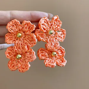 Detailed close-up of hand-woven orange raffia flower earrings with golden bead center