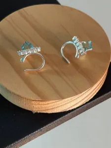 Macro view of silver-tone ear cuffs featuring blue square gemstones and zircons