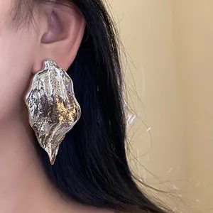 Close-up of large textured silver leaf earrings on model's ear showing elegant organic design