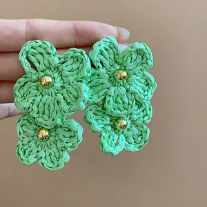Detail view of large green raffia flower earrings with golden bead accents for summer.