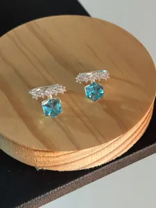 Close-up detail of square blue zircon ear clips on a natural wooden display stand