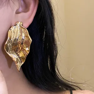 Macro detail of large golden crumpled leaf drop earrings with minimalist fashion design