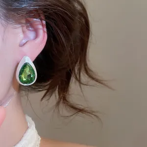 Close-up of vintage teardrop stud earrings with faceted green stone and brushed silver finish