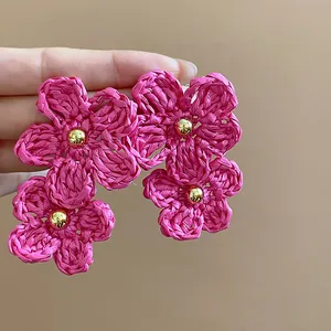 Detailed view of pink raffia flower earrings with gold bead centers and silver needles.
