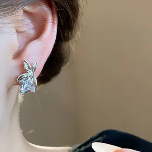 Primo piano di un orecchino a lobo in argento con zircone quadrato e design a fiore indossato.