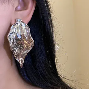 Close-up of a large textured silver leaf earring worn by a model, stylish jewelry detail