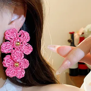 Close-up of vibrant pink woven raffia flower earrings with a golden center bead