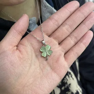 Close-up of a silver four-leaf clover pendant necklace featuring a green cat-eye stone