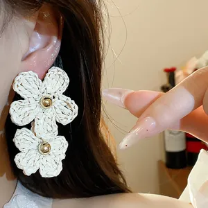 Detailed view of white woven raffia double flower earrings with a golden bead center