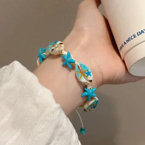 Close-up detail of blue starfish and white cowrie shell beaded bracelet on wrist