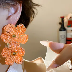 Close-up detail of orange raffia woven flower earrings with gold bead centers on model