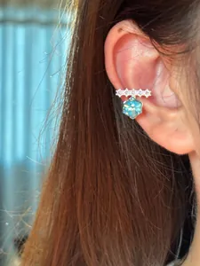 Macro view of a sparkling silver ear cuff with blue hexagonal stone and zircons on an ear