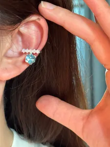 Detailed view of an elegant silver ear cuff with a dangling blue hexagonal stone.