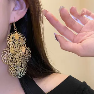 Close-up of golden hollow lace pattern on statement dangle earrings worn by model