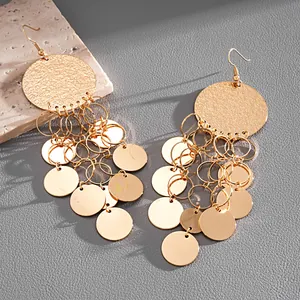 Detailed view of gold metal round sequin tassel earrings on a textured gray background