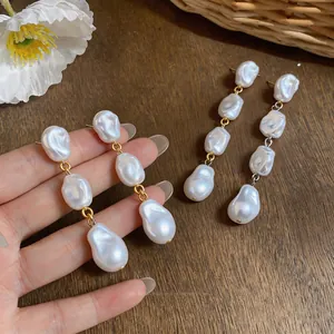 Eleganti orecchini pendenti con perle barocche irregolari su sfondo in legno rustico naturale