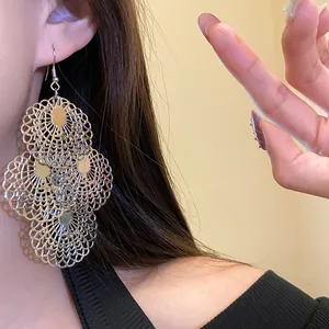 Close-up detail of large metallic filigree hollow-out drop earrings worn by a model