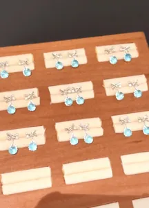 Detail of aquamarine teardrop zircon stud earrings with silver bow design on wooden tray