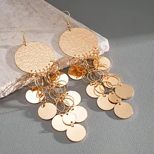 Close-up of gold-colored metal earrings with round textured studs and sequin tassels