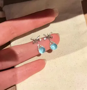 Detailed view of silver bow stud earrings with light blue round cubic zirconia