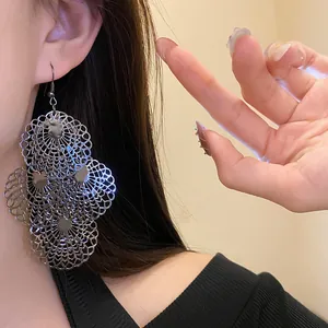 Close-up view of oversized silver filigree hollow tiered dangle earrings worn by a model