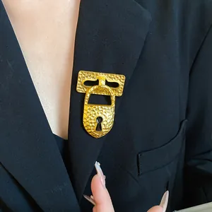 Detailed view of a vintage hammered gold lock brooch with keyhole on a black blazer